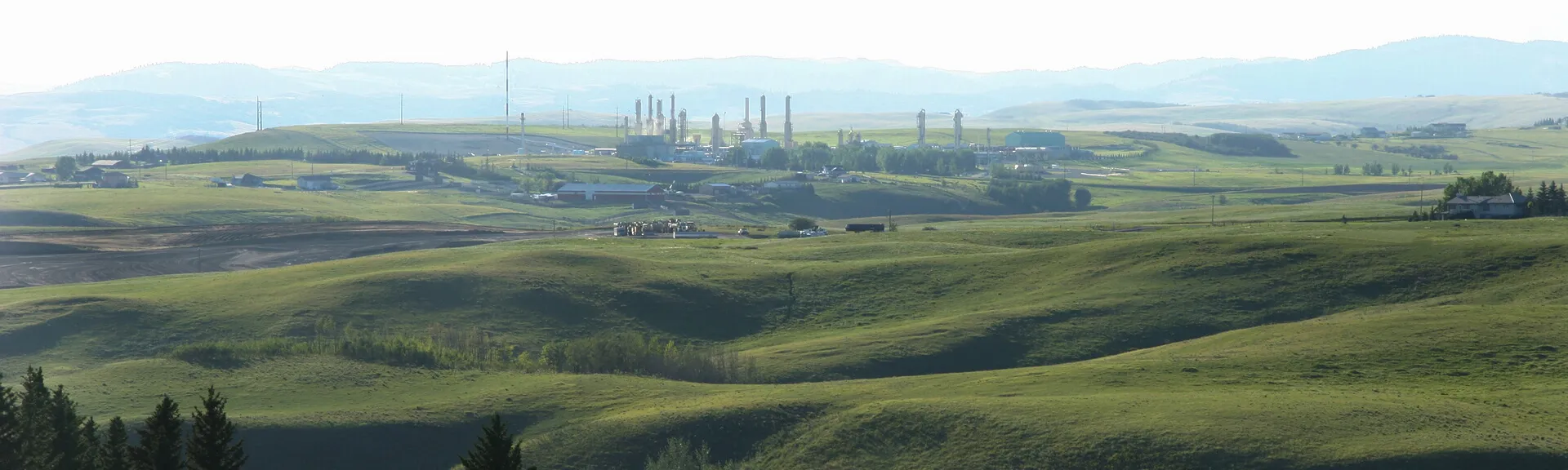 Green hills with distant industrial buildings and mountains